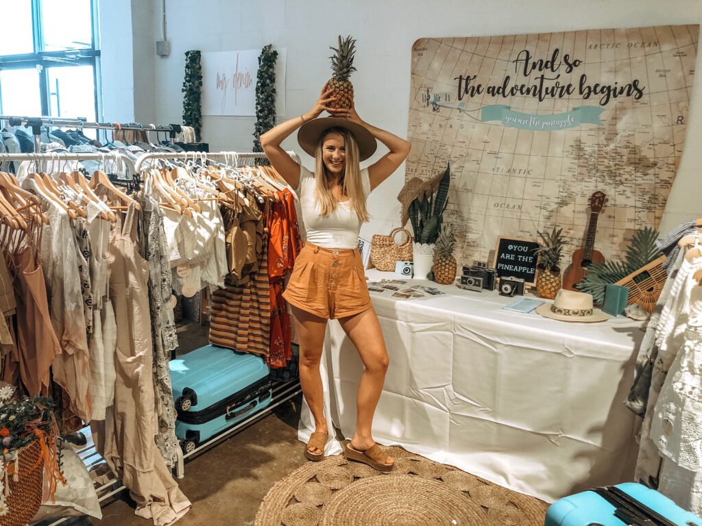 women holding pineapple in front of a clothing boutique market booth